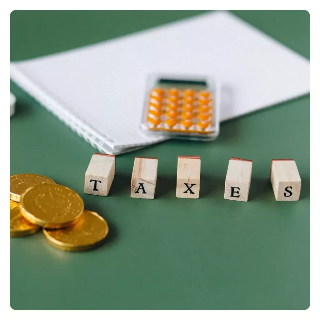 Top 10 Benefits of Hiring a Payroll Compliance Practitioner No One Will Tell You 1 wooden blocks spelling TAXES, accompanied by gold coins, a calculator, and a notebook on a green surface